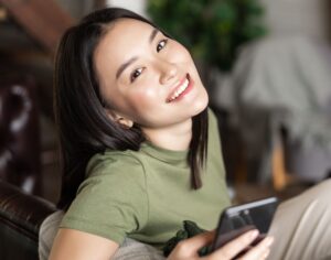 dreamy smiling asian woman using mobile phone sit 2021 12 09 20 53 13 utc 1 1